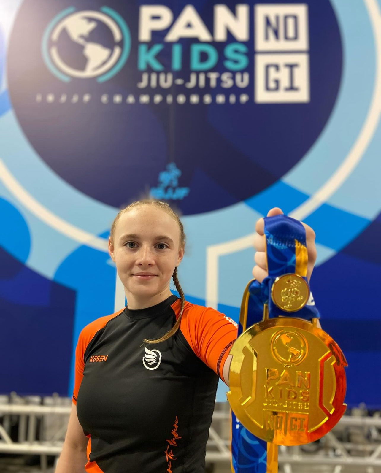 Gold medal photograph taken at the 2024 IBJJF Pan Kids No-Gi Championship. The medal bears the Pan Kids IBJJF Championship identification. The PAN KIDS NO-GI IBJJF CHAMPIONSHIP event backdrop is visible in the background.
